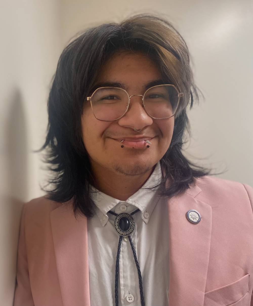 Image 1 of 2 Person standing in pink suit next to wall smiling